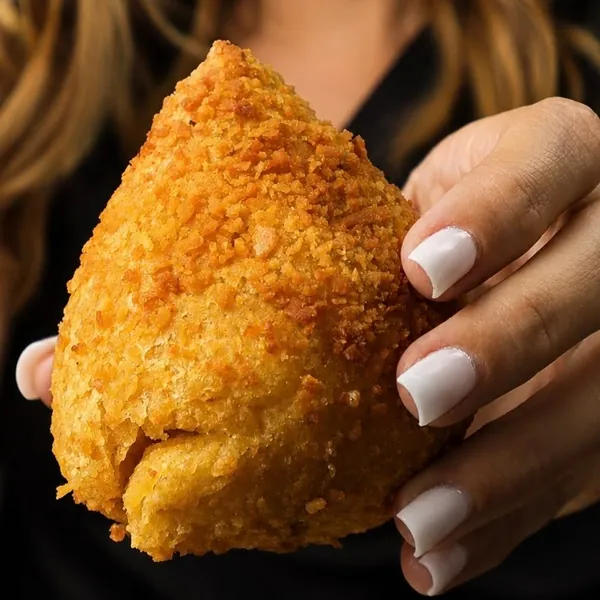 Mão segurando coxinha de massa de batata